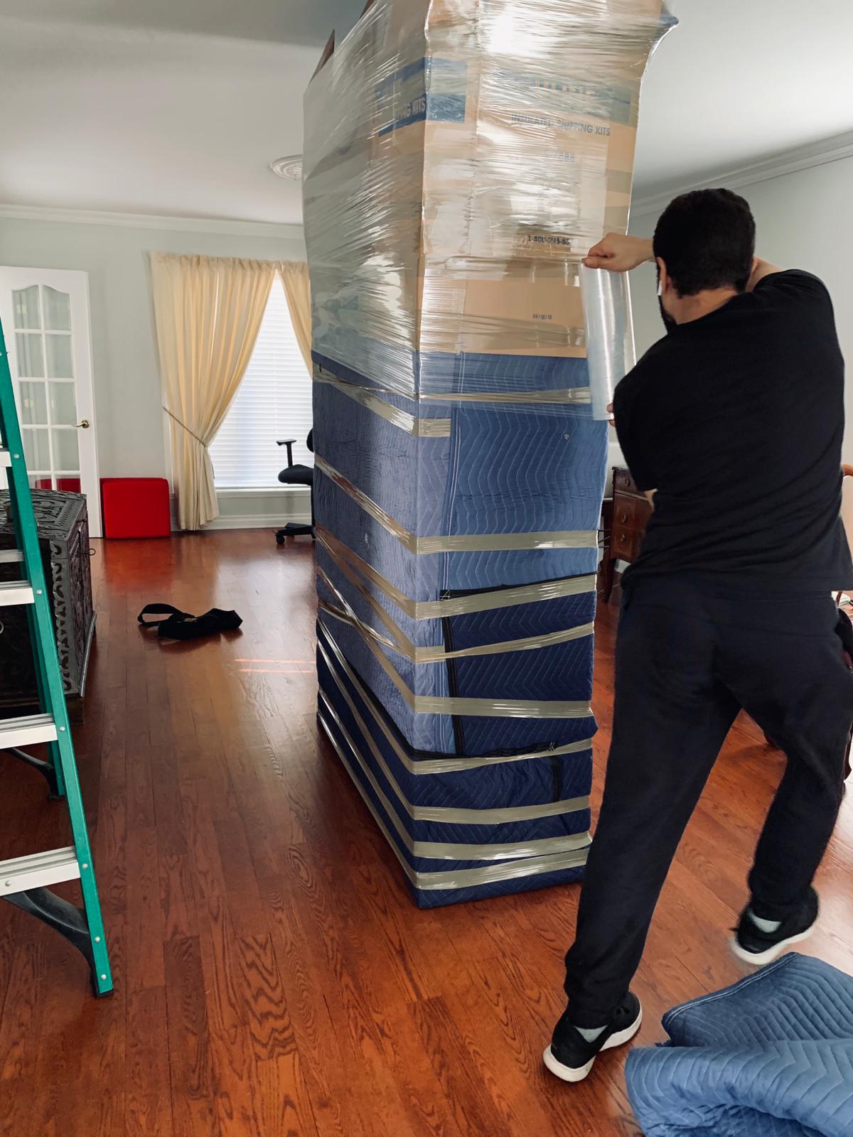 alt="A man wrapping a glass cabinet with protective material for moving"