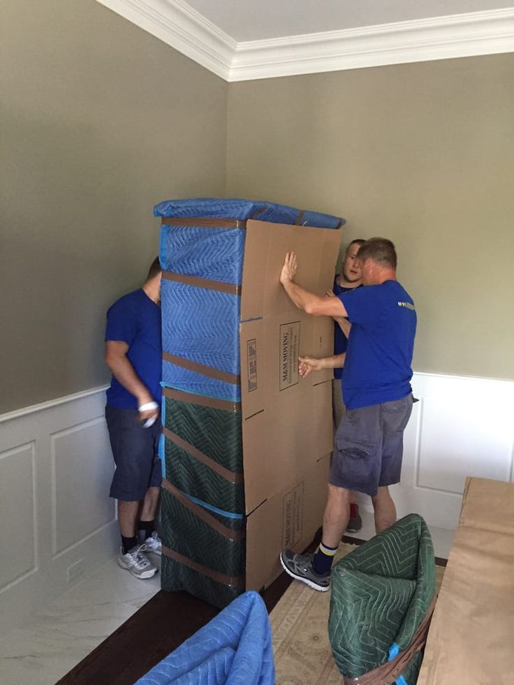 alt="three guys wrapping a glass cabinet with protective material for moving"