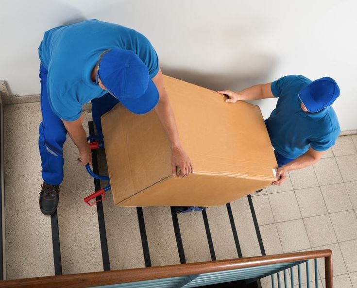 alt="Two men carrying a heavy box down the stairs"